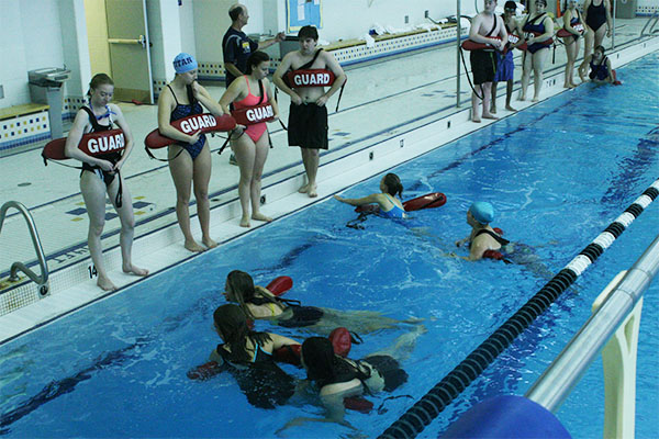 Lifeguards to the rescue:  Standing on the ledge of the pool, South lifeguards-in-training look upon their peers in the water as they demonstrate their newly learned skills. South students who took the course and became certified by the Red Cross were present at the free admissions section of Gilson Beach when senior James Kranzer* dove headfirst into Lake Michigan and suffered a spinal injury.