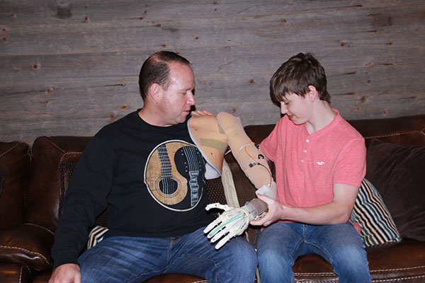 A Personal Touch:  Aiding his father, Michael Fine, in applying his 3D printed prosthetic arm, senior Jacob Fine explains the myoelectric prosthetic arm he had created for Michael. After Michael had been involved in a car accident and lost his left arm, Jacob decided to use his passion for engineering to construct a lightweight, efficient prosthetic for his father.
