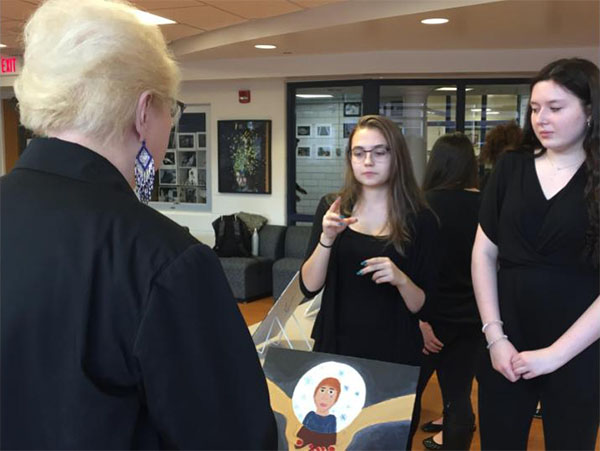 SIGNING   THROUGH   THE   SILENCE:   Bending their heads over their work (left), juniors Jordan Dahiya and Sarah Lothian attempt to convey some of the challenges of being deaf. Holding her hands in front of her (right), junior Kasia Dyrda explains her painting using sign language. The American Sign Language Art Gallery was held in the SAC on Thursday, Nov. 8.  