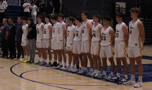 Standing Tall: Boys varsity basketball stands for the pledge of Allegiance before a game as they get ready for their next opponent. Before this matchup, the team values hard work and communication in order to secure the victory.