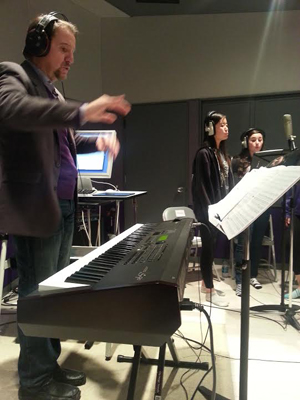 LIVE IN STUDIO: In the home studio of Gary Fry, VX Studio Vocal Ensemble (VX) director, sophomore Jewoo Kim and junior Julia Packer stand behind a microphone to record their part of the song Let It Go, a track from the animated Disney film, FROZEN. The VX members completed multiple takes of the recording to make sure each part was received perfectly to keep as a reference for their live practices. 