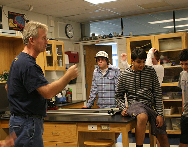 HUMOROUS HENDERSON: Demonstrating to his students the physics behind Newton’s first law of motion, Physics Teacher Tom Henderson lays on a bed of nails and has a student swing a sledgehammer onto a cinder block resting on his chest. In the picture to the left, Henderson instructs the students on how to perform their own version of the experiment.