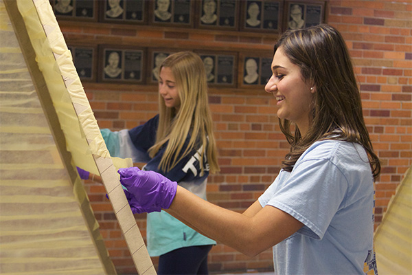 DECORATING DUO: Attaching a yellow streamer to support posts, juniors Danielle Callas and Bailey Burke lay the finishing touches on a pyramid for GBSís Turnabout dance, ìNight on the Nileî, on March 5. Callas and Burke participate in Girls Letter Club, a club for varsity female athletes, which is one of the many extracurricular activities offered at GBS.