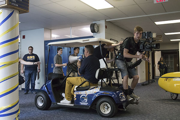 Leading   the   Lip   Dub:   Intently filming the 2016 lip dub, Jim Shellard, Student Activities director, and seniors Josh Noll, and George Gould use a golf cart to ensure the steadiness of the footage. The lip dub crew simulated the route every day for three weeks prior to the actual filming of the lib dub in order to guarantee minimal mistakes. 