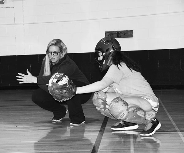 Friends   on   the   field:   Kneeling toward the ground, junior Winnie Tomsheck and Dana Boehmer, PE teacher and softball coach, go over technique for the catcher position. According to Tomsheck, she is appreciative of the bond she and Boehmer have formed through softball, which has led Tomsheck to look up to her coach as a role model. Photo by Sophie Mason