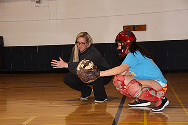 Coaching a player, Dana Boehmer crouches down to help junior Winnie Tomsheck with her catch. This is Boehmers first year coaching varsity softball