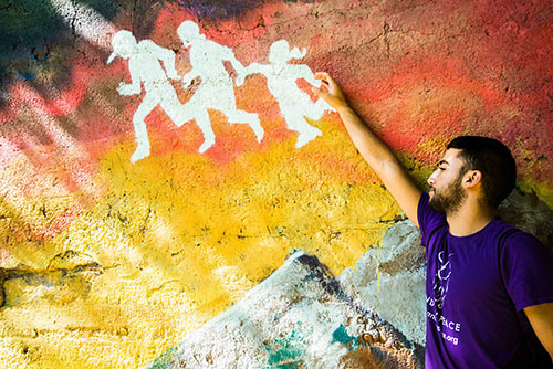 INTERFAITH FRIENDS:   Observing art in Pilsen, a neighborhood in Chicago, Liad, a Jewish Israeli, connects to a particular image by holding hands with figures in the mural (right). 