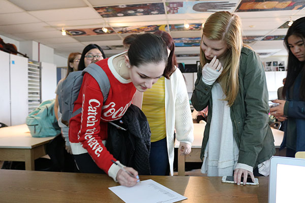 PRODUCTIVE POWWOW:  Leaning over a table, senior Angela Golota and junior Oliva Wilas sign into a National Art Honors Society meeting. Stephanie Fuja, fine arts teacher, brought a chapter of the National Art Honors Society to South this year to bring attention to art students’ work. 