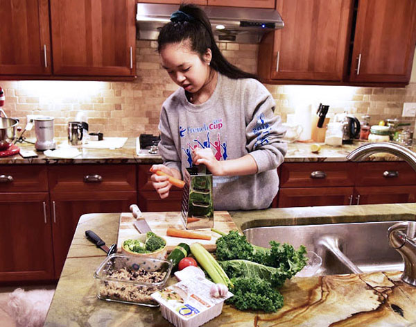 SLICIN’ AND DICIN’: Grating a carrot, junior Rachel Luo prepares vegetables for her tofu scramble. Luo enjoys cooking healthy recipes as a way of relieving stress, while also being able to incorporate raw and organic foods into her diet. 