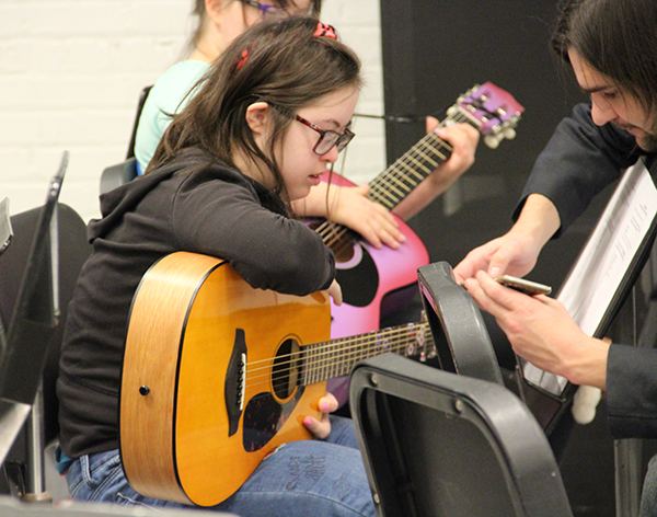 Guitar Guru: Resting her arm on the guitar, freshman Molly McNamara learns how to play with the help of Teacher’s Assistant Jacob Lill. Guitar is a music elective that is offered at South that gives students the freedom to learn several songs of their choice. 
