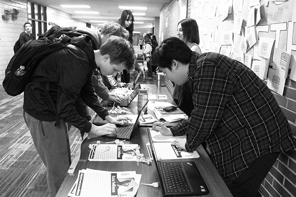 Signing   for   solimon:   Leaning over the Amnesty table, freshman Michael Cunningham (left) adds his name to a petition supporting Azza Solimon, a human rights activist for victims of torture, domestic abuse and rape, who was recently arrested in Egypt. The petition will be sent to the President of Egypt to urge him to drop the charges. Photo by Nicole Surcel