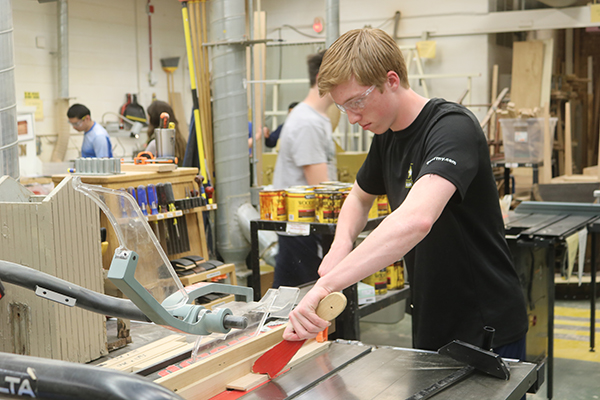 Holding a push stick to keep a piece of wood steady, sophomore Hunter Weisensel prepares to cut the wood for his project. There are four levels of woodworking offered at South.