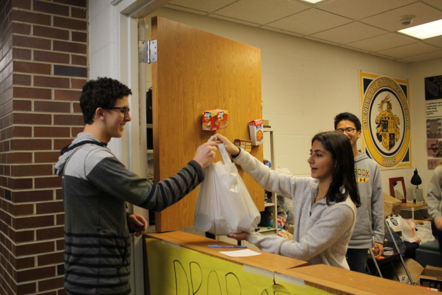 Handing+Laya+Anvari%2C+senior+class+representative%2C+a+bag+of+donations+for+the+Food+Drive%2C+senior+Ben+Kalish+helps+provide+supplies+for+568+families+around+the+community.+The+food+drive+underwent+a+number+of+changes+this+year+to+emphasize+the+humanitarian+aspect+behind+the+donations.+