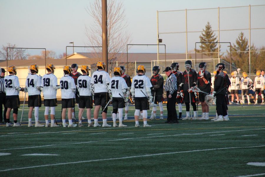 Lining up at center field, the boys lacrosse team stands together at the start of a game in the 2019 season.