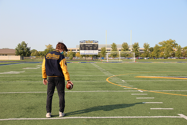 Melancholy Michael: Standing alone on the football field at John Davis Stadium, Varsity Quarterback Michael Bauer contemplates the arrival of his season. Because of IHSA regulations as a result of the coronavirus pandemic, the South football season will begin in February of this school year instead of August like normal
