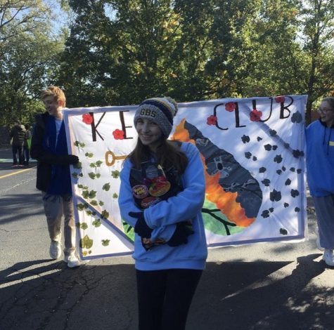  Serving the Community: Sloane Shabelman, as a sophomore, marches with Key Club at the 2019 homecoming parade. Standing in front of the banner, she passes out candy to other atendees.