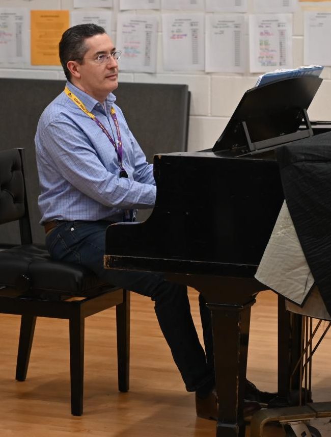 COOL KEYBOARD CLICKING: Sitting at the piano, Collaborative Accompanist Gregory Shifrin plays a warm-up for Glee Club as they sing along. Playing the simple accompaniment for the vocal warm-ups allows the choir to prepare their voices for more complex pieces later on in the rehearsal.