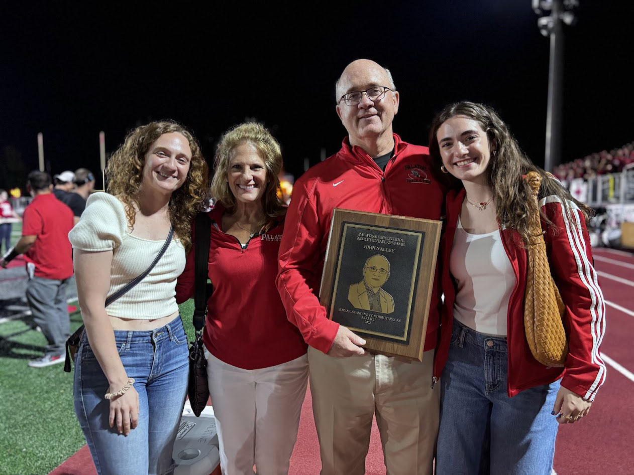 PALATINE PRIDE: John Nalley (middle right) stands on the Palatine High School outdoor track holding the plaque recognizing him as a member of the Palatine Hall of Fame. He posed with his eldest daughter Mary Patricia Nalley (left), his wife Anne Marie Nalley (middle left), and his youngest daughter Margaret Nalley (right). 
Photo courtesy of John Nalley