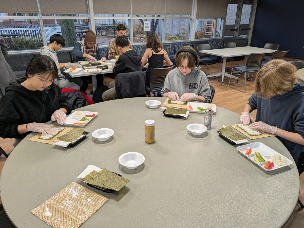 SUSHI WORKSHOP ROLLED UP: Sophomores Michelle Sugarsuren and Eva Koster (pictured left to right) spread a thin layer of rice over their nori to prepare sushi rolls during Japanese class’s sushi workshop in the Student Activities Center. Japanese Teacher Mai Bryans has continued on this tradition from previous teacher Yasuko Makita to immerse students in culture by teaching them the basics of making sushi. Photo by Mai Bryans