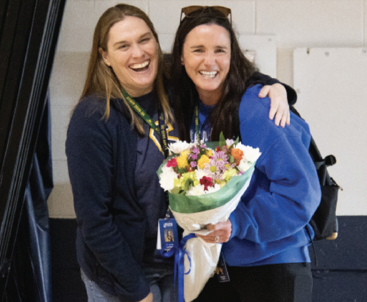 LEADING BY EXAMPLE: Principal Dr. Barbara Georges (left) surprises Meaghan Fastert (right), P.E. Teacher and Distinguished Teacher of the Year, with a bouquet of flowers to signify her achievement. After receiving the flowers, Fastert was met with balloons and desserts delivered by Joshua Stanton, P.E. Instructional Supervisor.