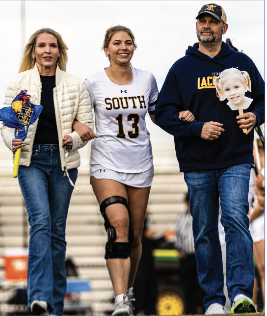 SENIOR NIGHT: Senior Townsend Walter (center) walks down the field with her parents, Carol Ann McCartney (left) and Craig Walter (right) at senior night on May 5. All three are seen arm-in-arm, reflecting on Walter’s past years on lacrosse. 