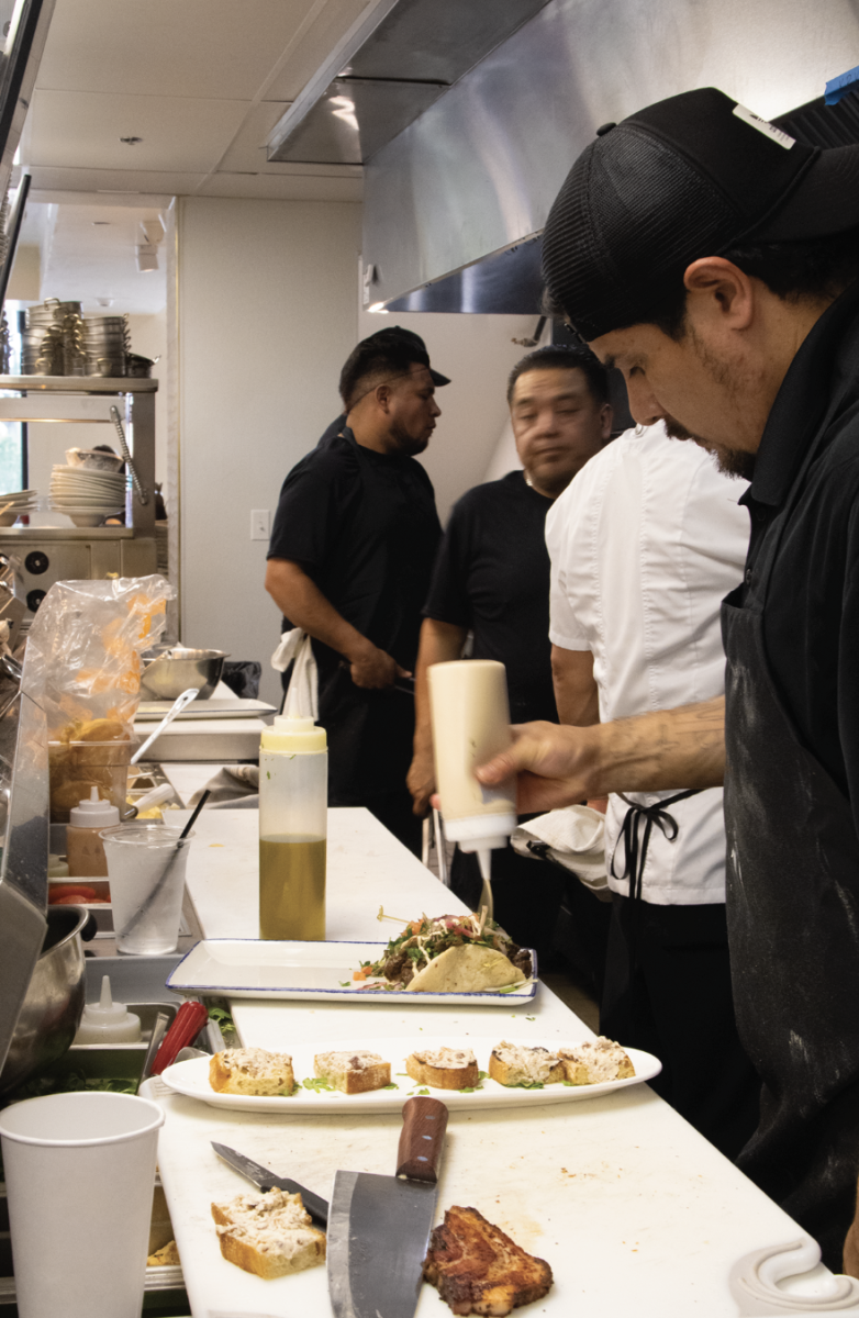CULINARY HUSTLE AND BUSTLE:  Chefs at The Foxtail work together to prepare various coastal dishes. This chef finalizes a taco dish with a sauce.
